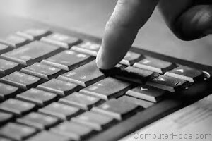 Finger pressing down on the enter key of a computer keyboard.
