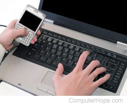 Person holding a smartphone and using a laptop.